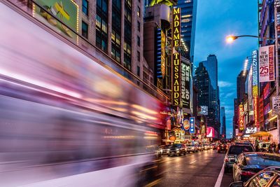 Blurred motion of bus amidst cars on illuminated street at night