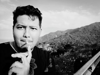 Portrait of young man holding mountains against sky