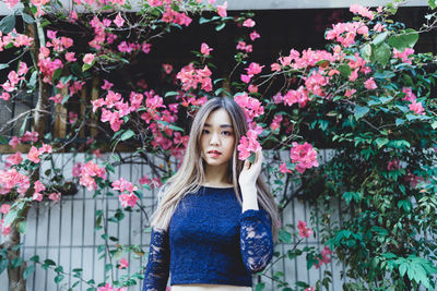 Portrait of beautiful young woman standing by pink flowers