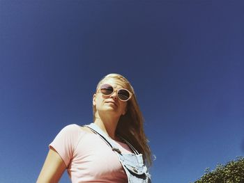 Low angle view of young woman against clear blue sky