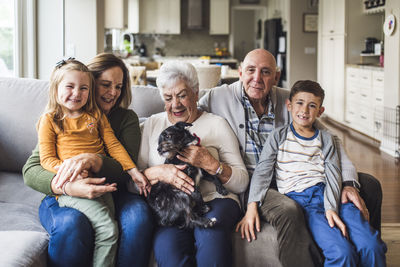 Multigenerational family and small dog sitting on living room couch