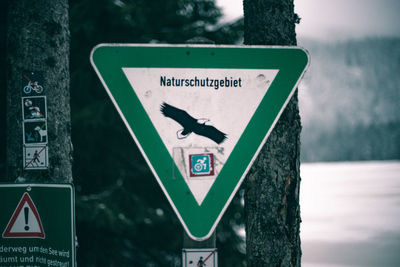 Close-up of road sign against tree trunk during winter