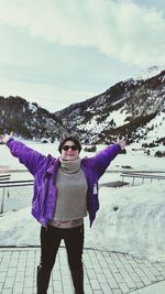 Woman with arms outstretched standing on footpath against snowcapped mountains