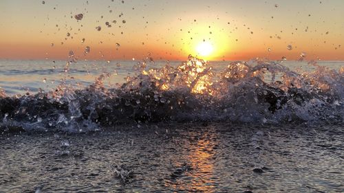 Water splashing in sea against sky during sunset