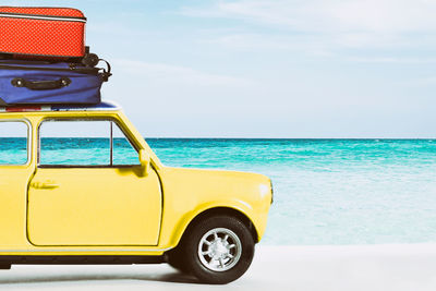 Luggage on vintage car at beach against sky