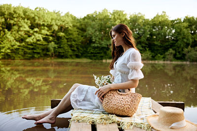 Side view of woman sitting on bench against lake