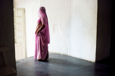 Rear view of woman standing against wall at home