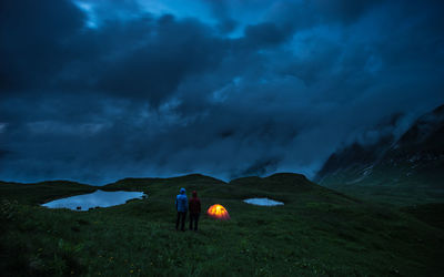 Rear view of friends standing on mountain against cloudy sky