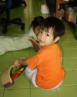 Portrait of boy holding musical instrument by sister on tiled floor at home