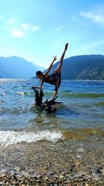 Full length of woman practicing yoga on driftwood in lake against mountains