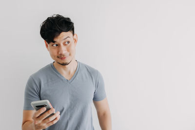 Young man looking away while standing against white background