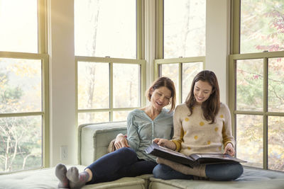 Smiling mother and daughter looking at photo album in living room