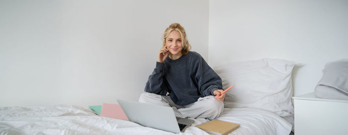 Side view of woman sitting on bed at home