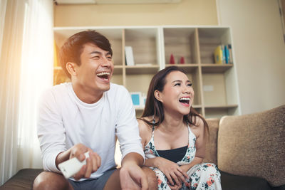 Happy couple watching tv while relaxing on sofa at home