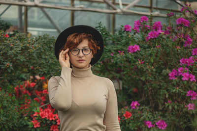 A beautiful plus size girl in eyeglasses and hat smiling among the green plants and flowers.