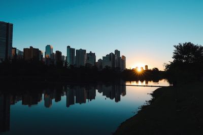 Reflection of silhouette trees and buildings against sky during sunset