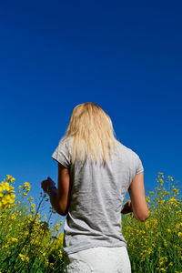 Rear view of young woman standing by plants on field against clear blue sky