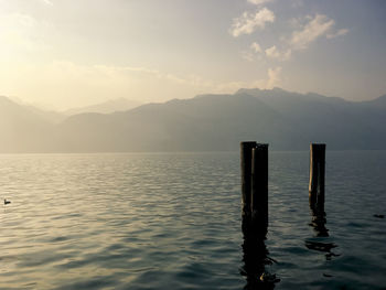 Wooden posts in sea against mountains