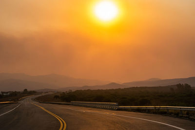 Road by mountains against sky during sunset