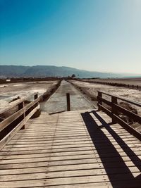 Boardwalk leading towards mountains against clear blue sky