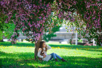 Girl sitting on grass against tree trunk