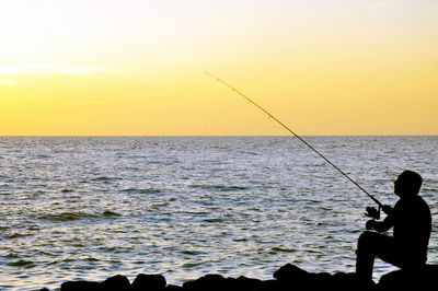 Man fishing in sea at sunset
