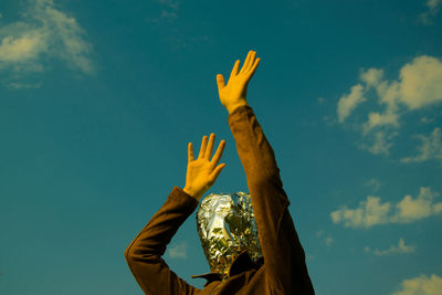 Low angle view of woman with covered face standing against sky