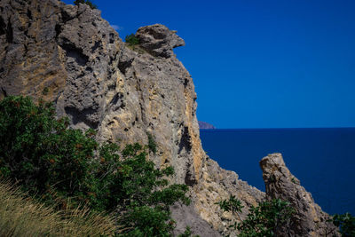 Scenic view of cliff by sea against clear blue sky