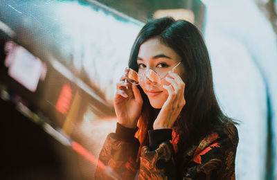 Portrait of young woman standing against illuminated city at night