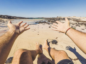 Low section of people on beach against clear sky