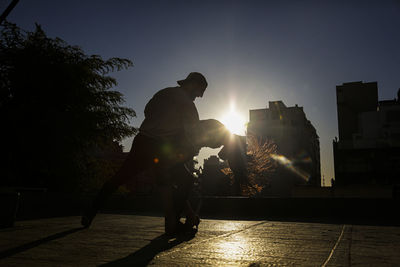 Silhouette man against bright sun in city against sky during sunset