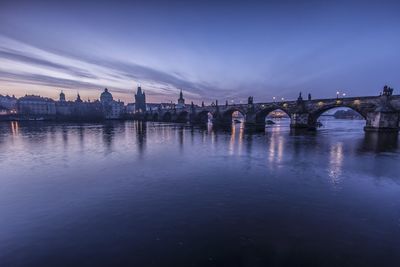 Charles bridge over river in city against sky at dusk