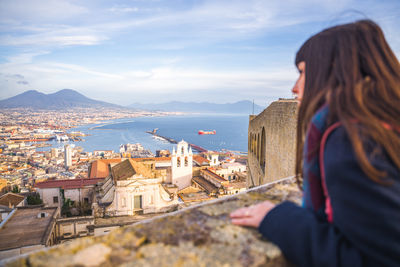 Rear view of woman looking at townscape by sea against sky