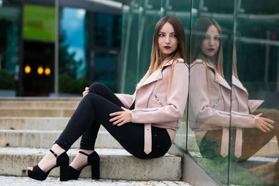 Young woman sitting on steps by glass building