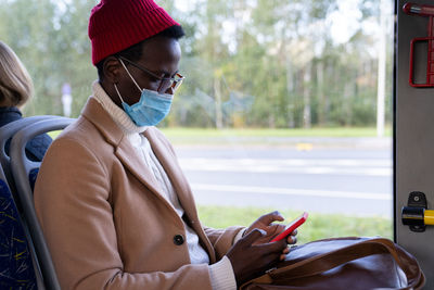 African passenger man using cellphone wear face mask sitting in public bus. covid-19, transportation