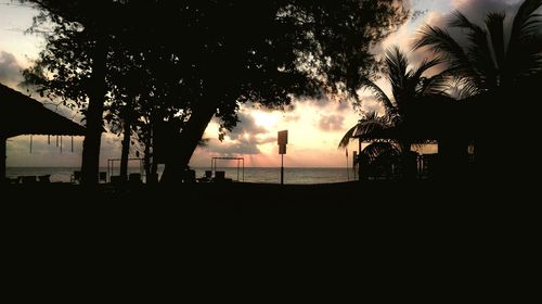 Silhouette palm trees by swimming pool against sky during sunset