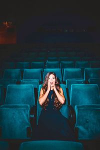 Shocked young woman looking away while sitting on seat in theater