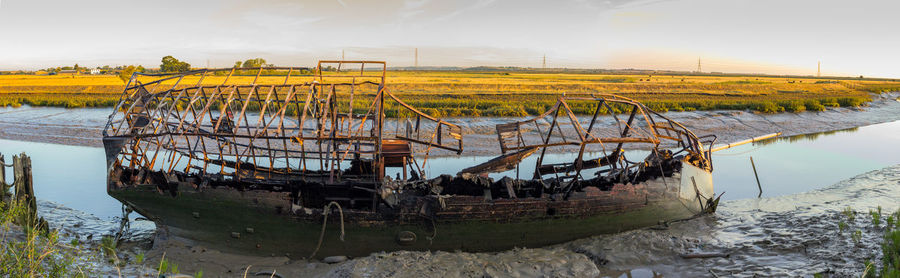 Abandoned boat moored on river against sky