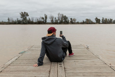 Rear view of woman sitting on pier against sky