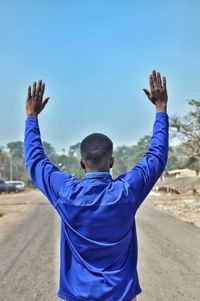 Rear view of man with arms raised standing against sky