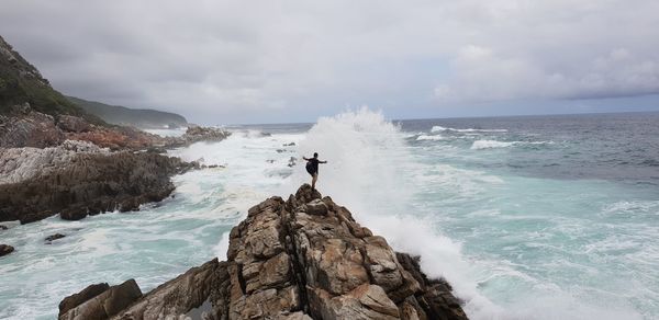 Man standing on rock by sea against sky