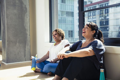 Happy female friends sitting against window in yoga studio