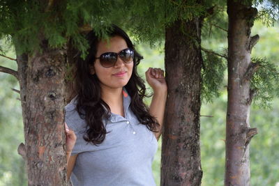 Portrait of young woman standing by tree trunk in forest