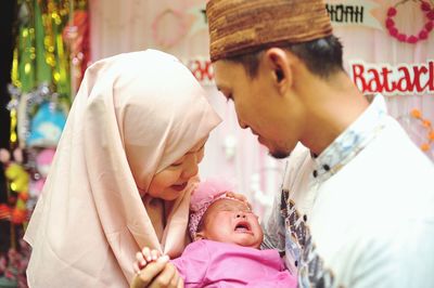 Baby crying on father's lap and being watched by her parents