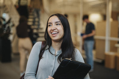 Cheerful female student carrying file folder at university