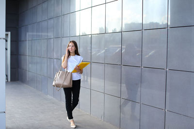 Young businesswoman talking on mobile phone while standing by wall