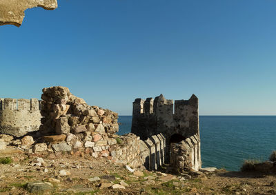 Old ruin by sea against clear blue sky