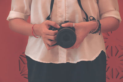 Midsection of woman holding red while standing against wall