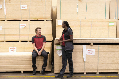 Smiling sales staff communicating with each other near plywood stack at warehouse