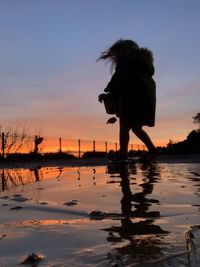 Silhouette woman standing at beach against sky during sunset